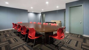 Une salle de conférence avec une table ronde, des chaises rouges et un sol recouvert de moquette.