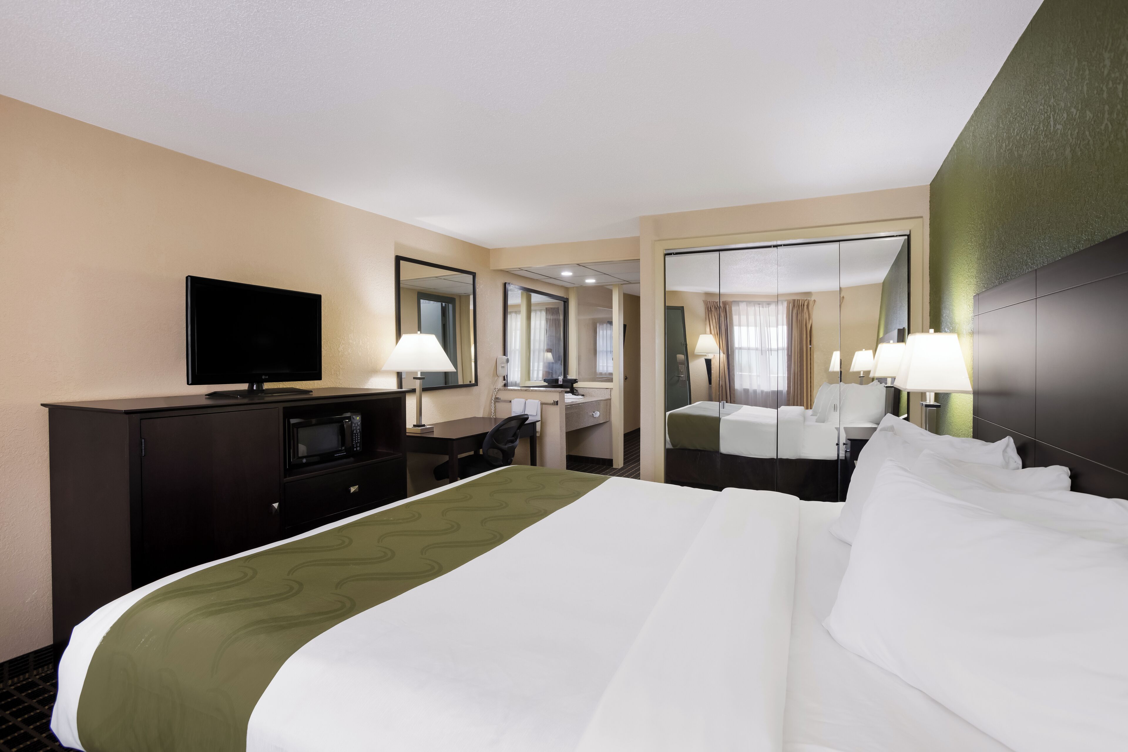 A hotel room with a large bed, a desk, a television, and a mirror.