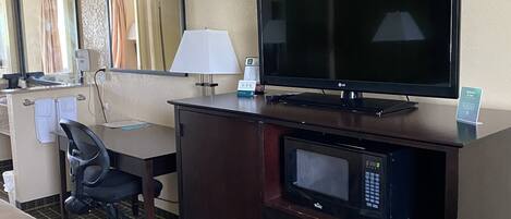 Een hotelkamer met een bed, een bureau met een televisie, een magnetron en een stoel.