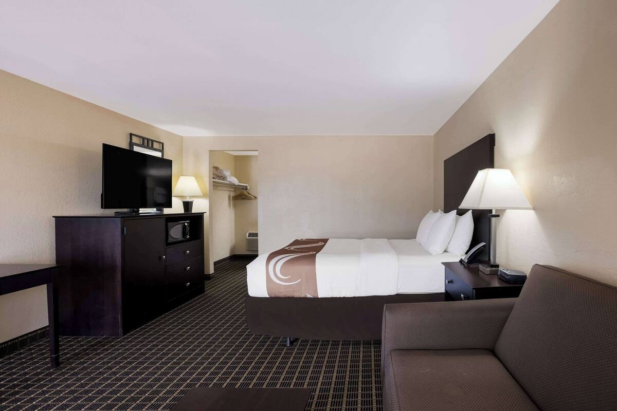 A hotel room with a bed, a desk, a television, a lamp, and a couch.