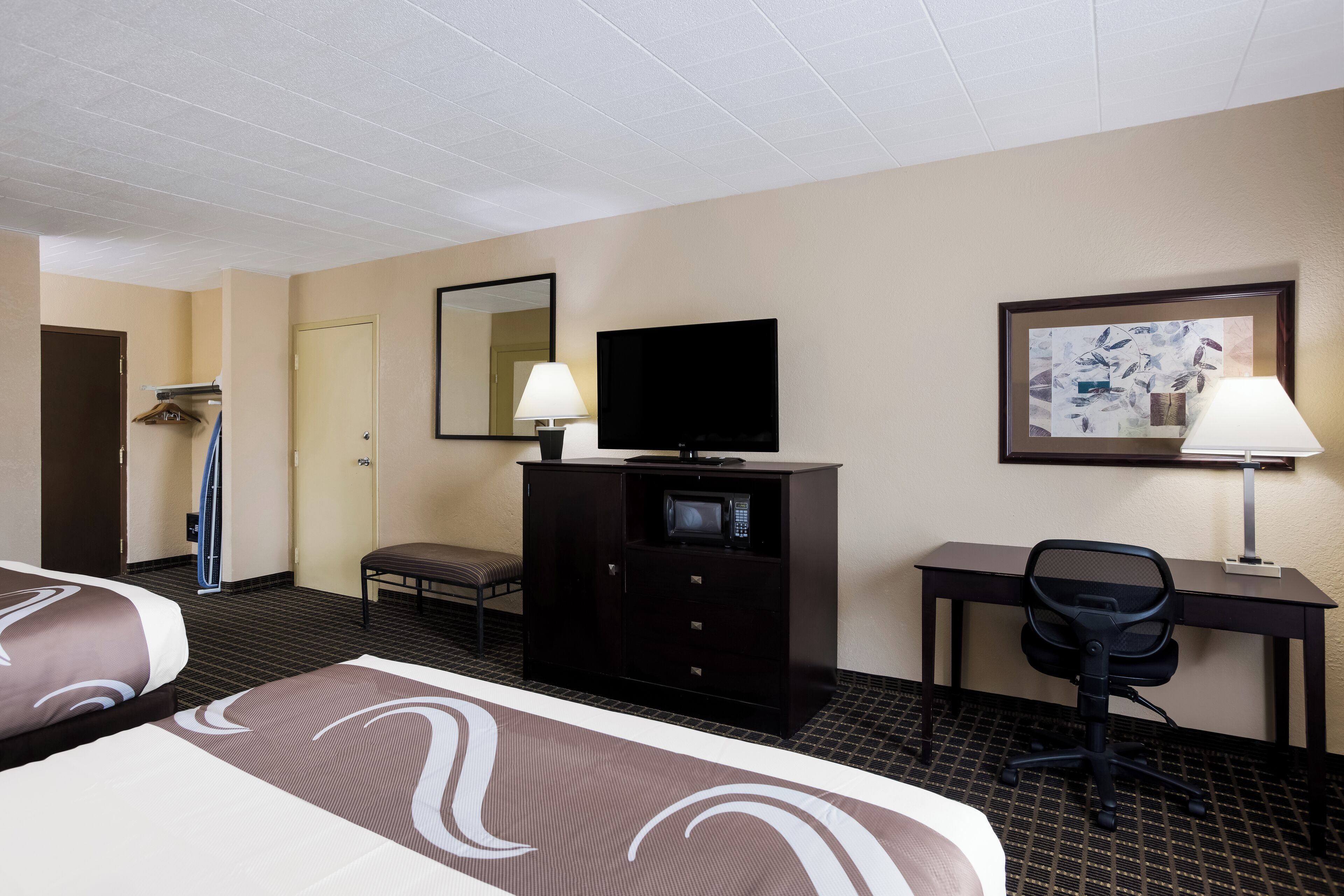 Una habitación de hotel con dos camas, un escritorio con computadora, televisor, silla y microondas.