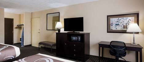 A hotel room with two beds, a desk with a computer, a television, a chair, and a microwave.