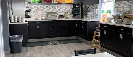 A modern kitchen with dark cabinets, a white countertop, and a dining area with a table and chairs.