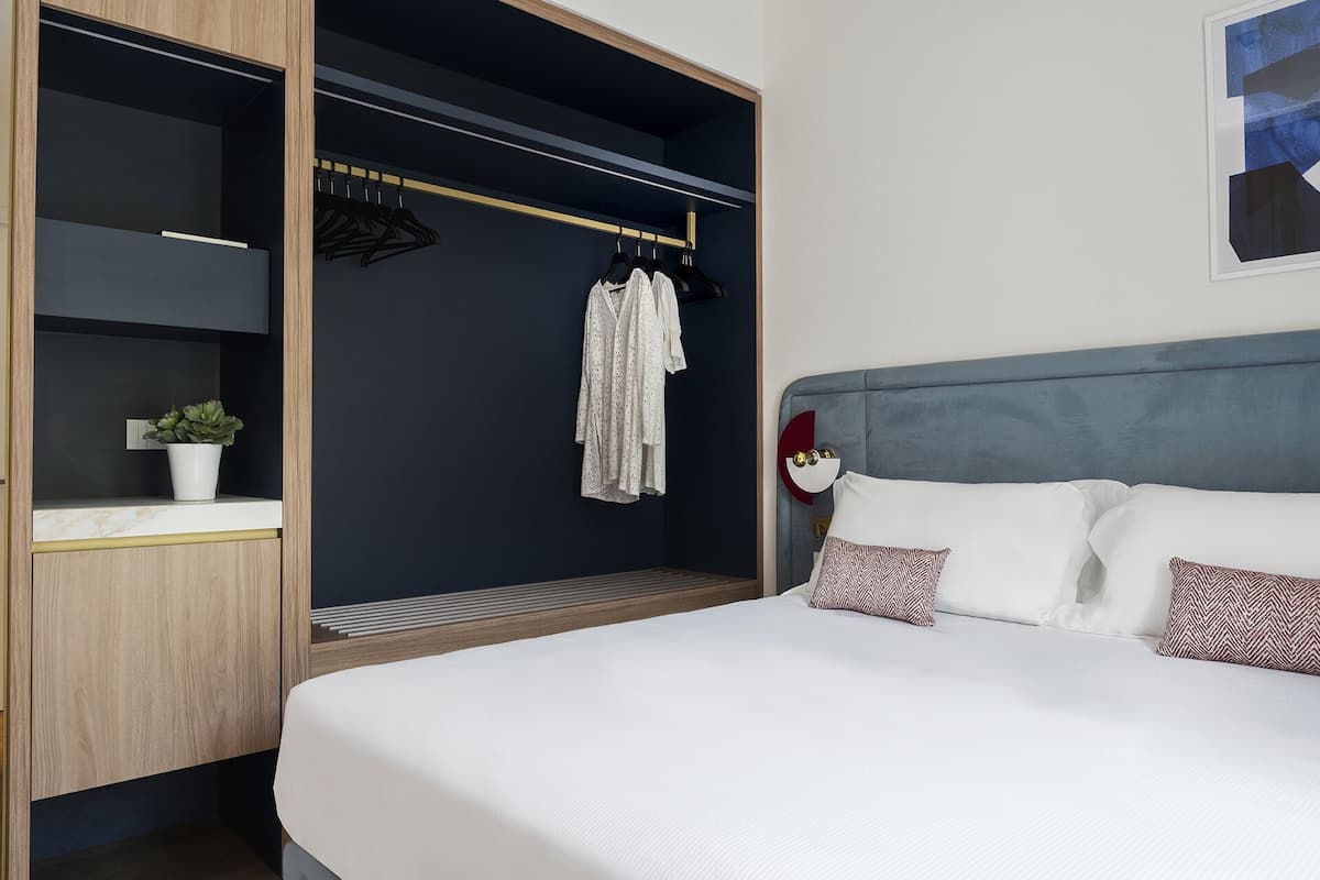 A hotel room with a bed, a wardrobe, a hanging rack with clothes, and a small potted plant.