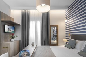 A modern hotel room with a large bed, a flat-screen TV, a desk with a plant, and a large window with curtains. - Villa Bianca (Rimini)
