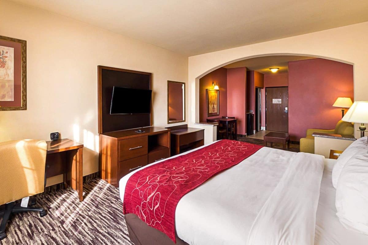 A hotel room with a bed, desk, chair, TV, and a small table.