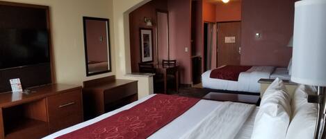 A hotel room with a large bed, a desk, a chair, a television, and a mirror.