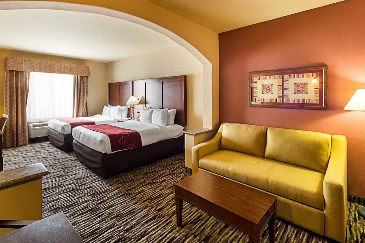 A hotel room with two beds, a sofa, a coffee table, and a framed artwork on the wall.