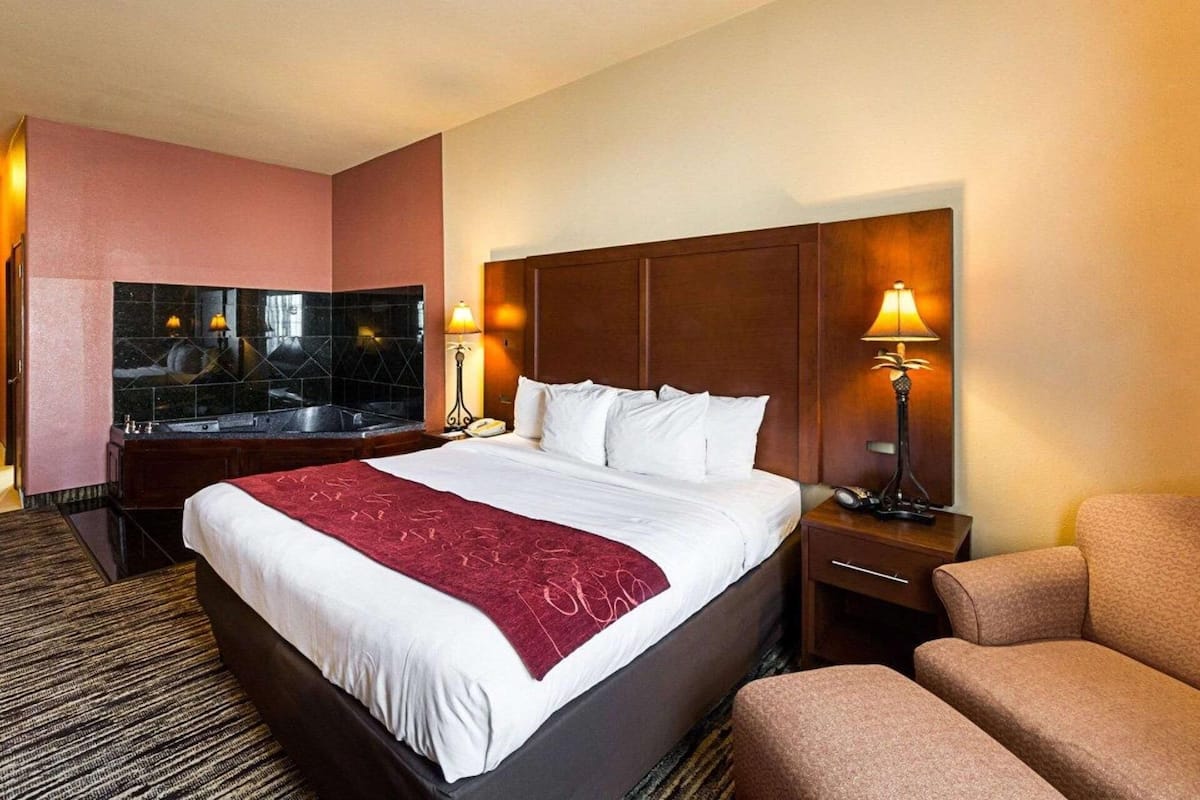 A hotel room with a large bed, a sitting area, a desk, and a mirror.