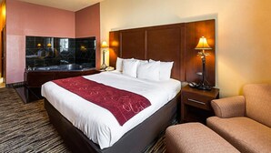 Quarto de hotel com uma cama grande, cabeceira de madeira, área de estar com uma poltrona, escrivaninha e espelho.