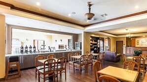 Um restaurante com cadeiras e mesas de madeira, um espaço de bar com diversos equipamentos e uma área de estar com sofá e poltronas.