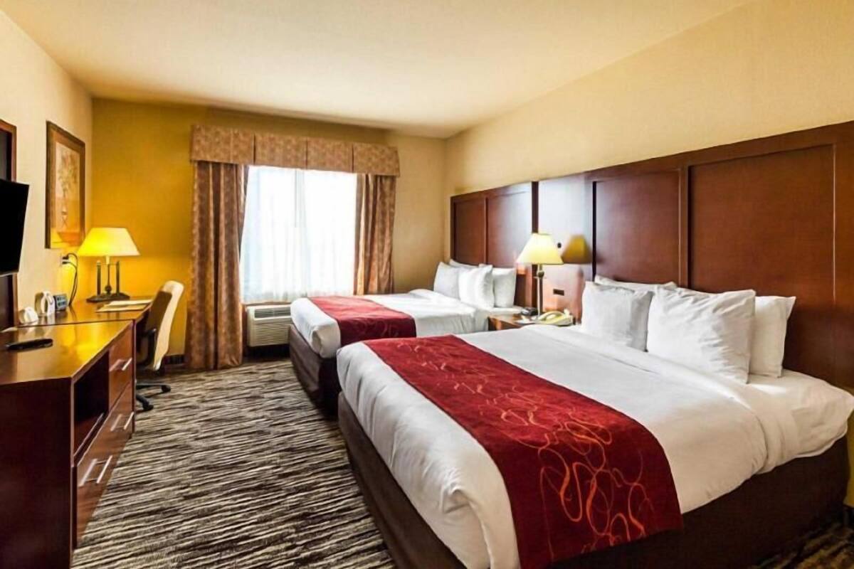 A hotel room with two beds, a desk, a chair, a TV, and a window with curtains.