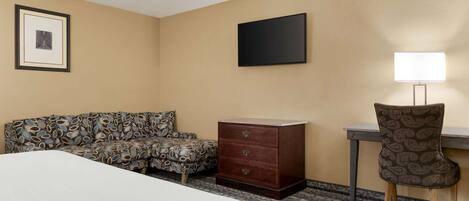 Habitación de hotel con cama, sofá estampado, cómoda de madera, escritorio con lámpara y un cuadro en la pared.