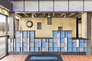 Zona de recepción con mostrador de baldosas, un reloj y un letrero de 'Travelodge'.