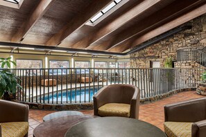 Un espace piscine intérieur avec un mur en pierre, un escalier et des sièges disposés autour de la piscine.