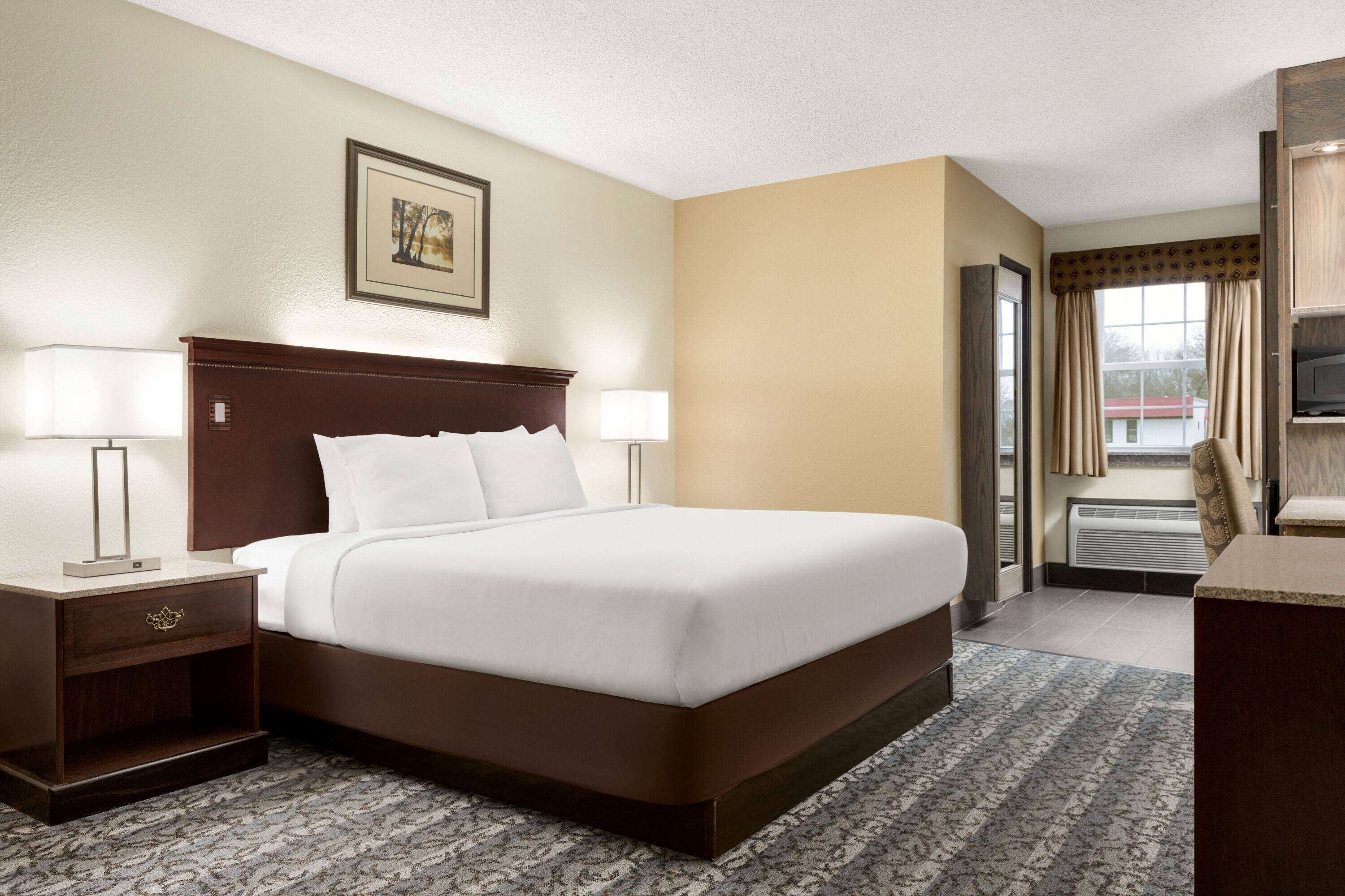 A hotel room with a large bed, two bedside lamps, a framed picture on the wall, and a window with curtains.