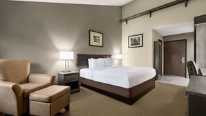 A hotel room with a large bed, a chair, a desk, and a door. - Travelodge by Wyndham Coffeyville (Coffeyville)