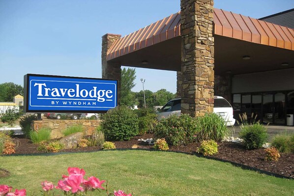 Un panneau indiquant un hôtel Travelodge, avec une structure en pierre et un espace de stationnement couvert.