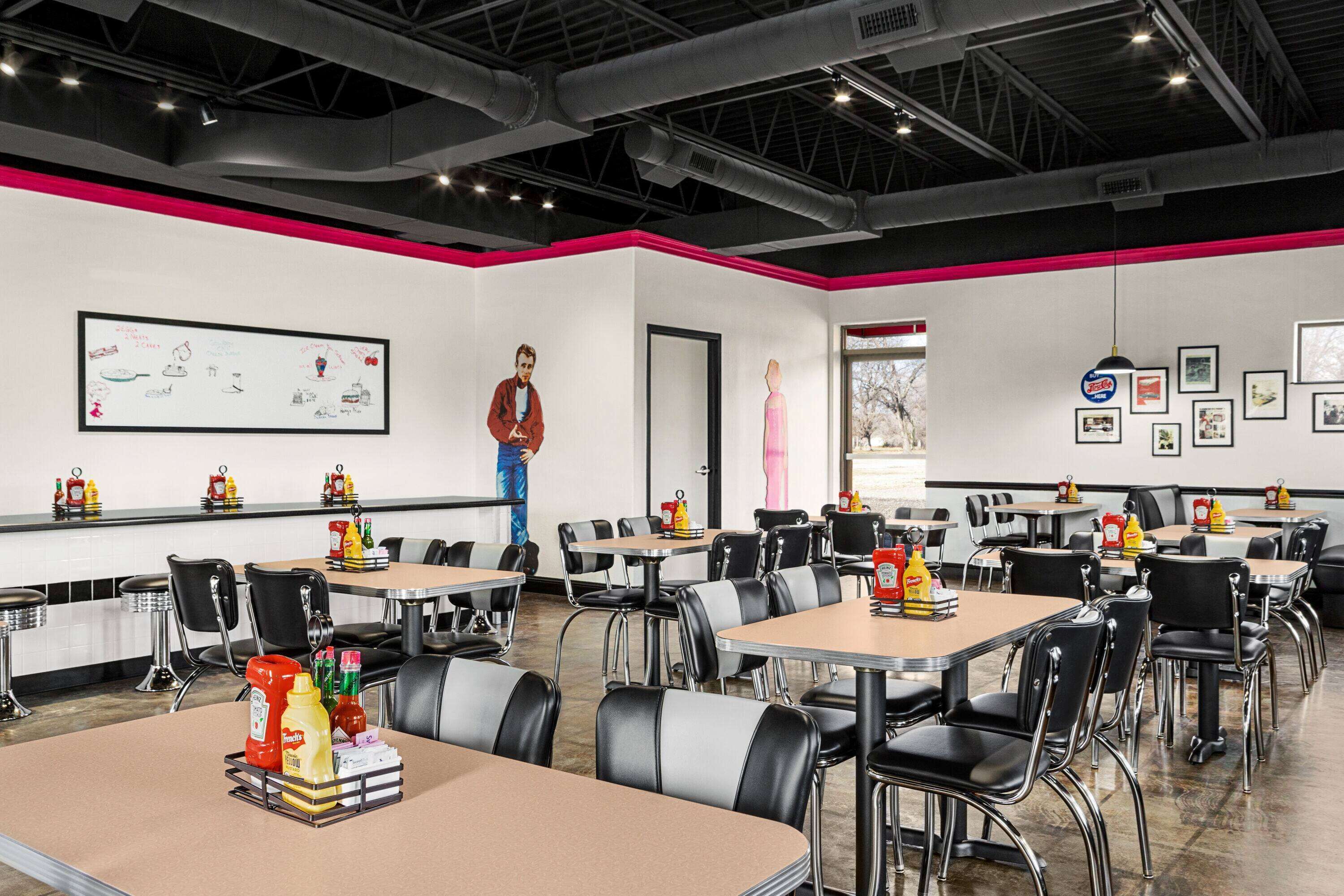 A modern dining area with tables and chairs, a whiteboard with drawings, and a person standing near the door.