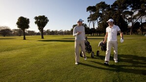 Zwei Personen auf einem Golfplatz mit Golftasche und Wagen.