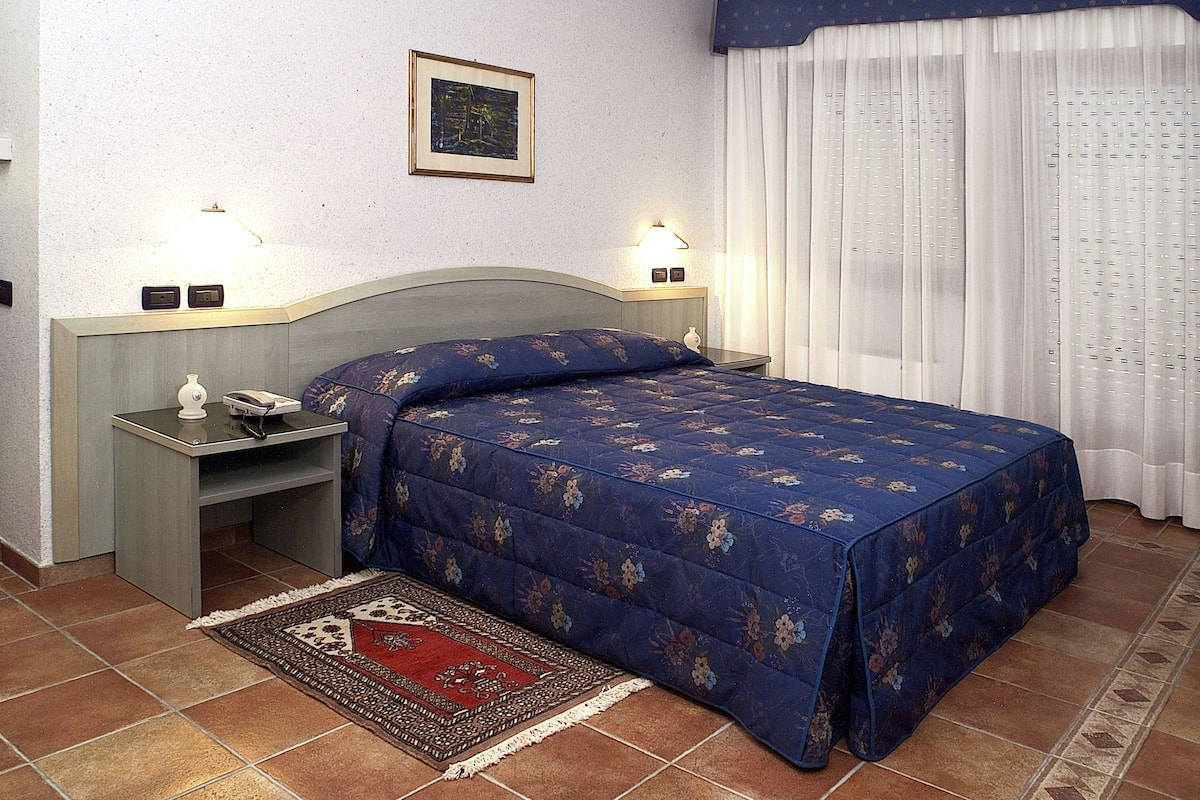 A bedroom with a bed, bedside tables, a nightstand, a rug, and a window with curtains.