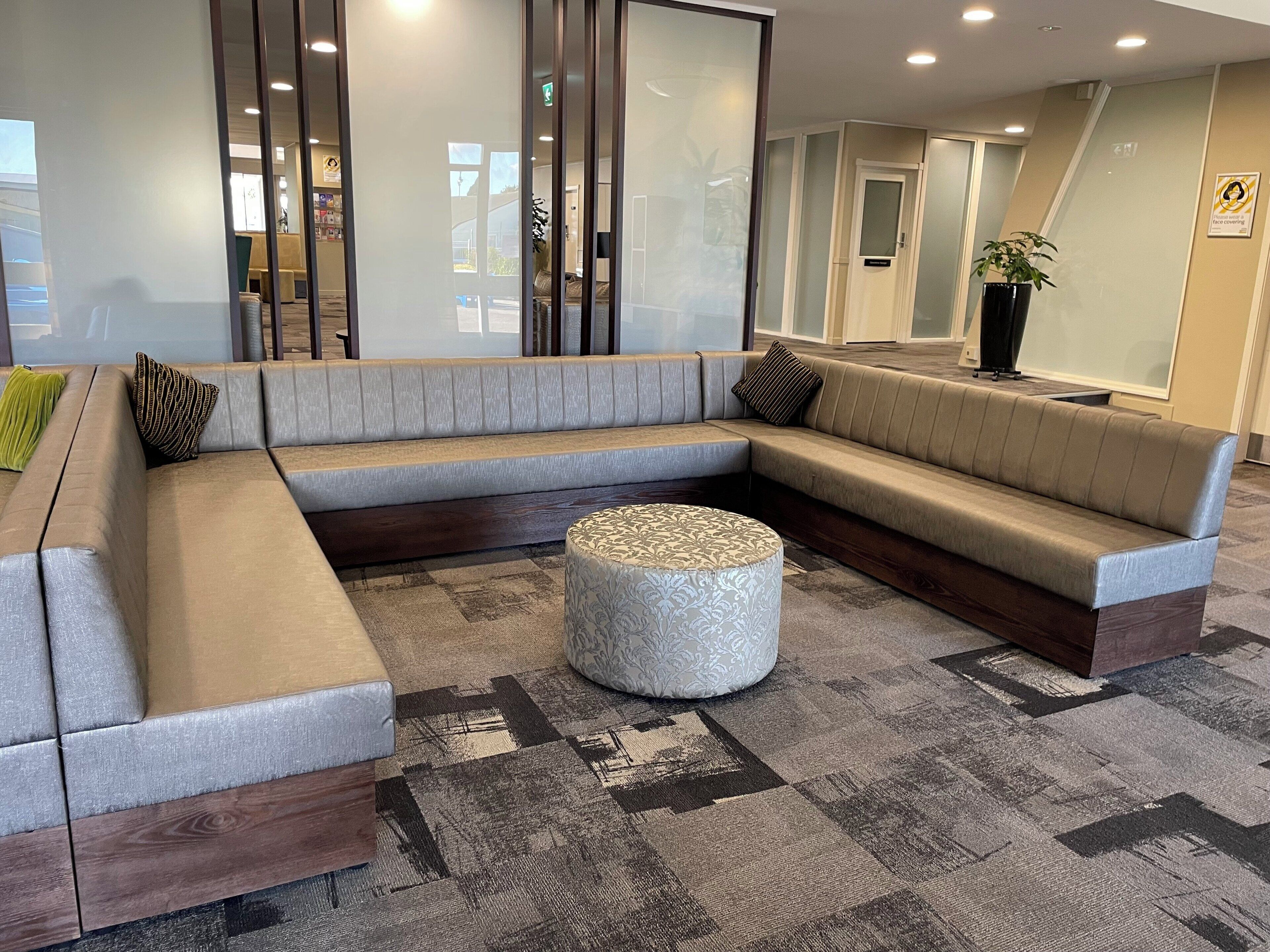 A modern lounge area with a sectional sofa, a round ottoman, and a patterned rug.