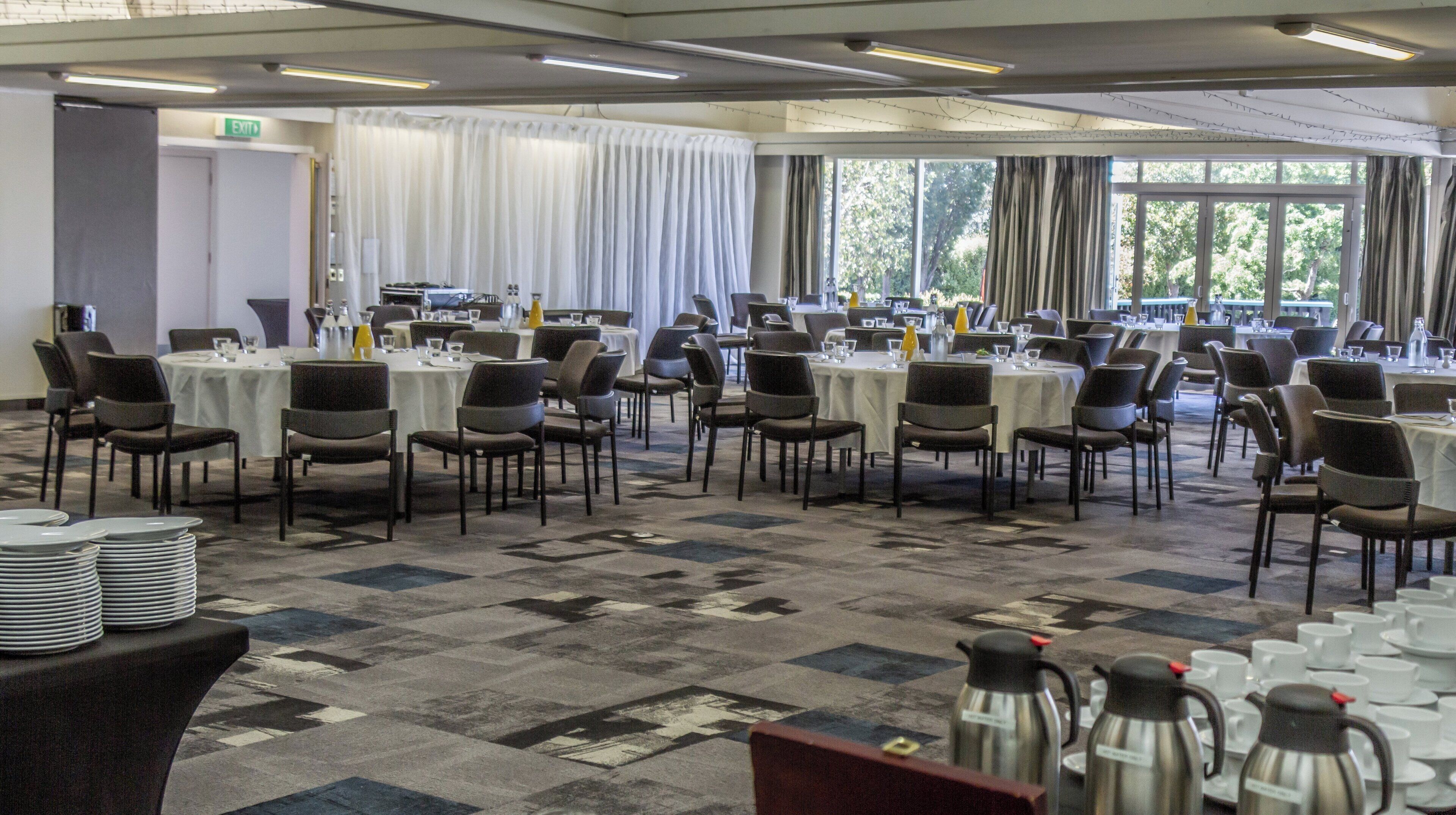 A conference room with multiple tables and chairs, a buffet area with food and drinks, and a view of trees through large windows.