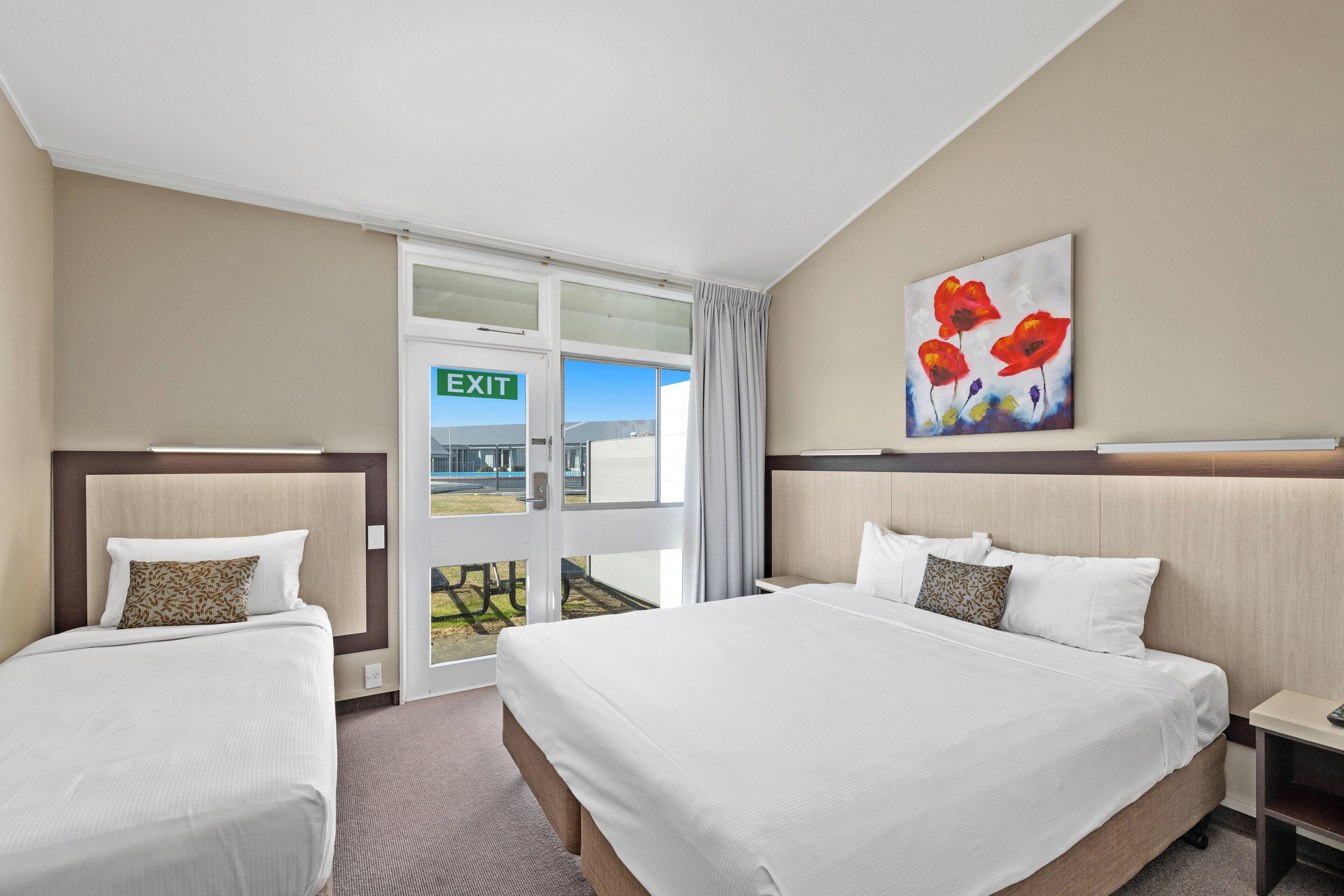 Habitación de hotel con dos camas, un cuadro de flores rojas y una señal de salida.