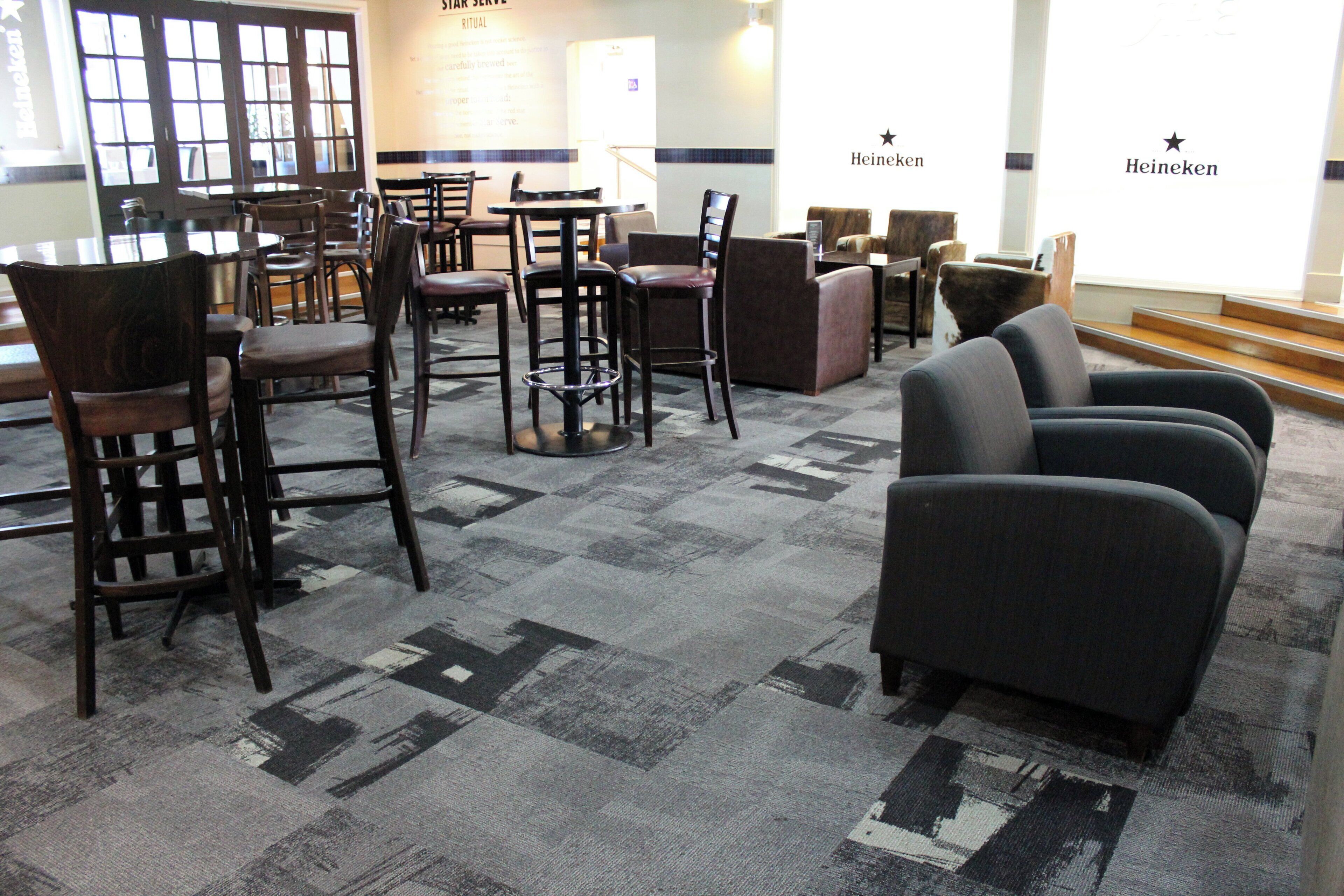 A hotel lobby with multiple seating areas, including bar stools and sofas, and a carpeted floor.