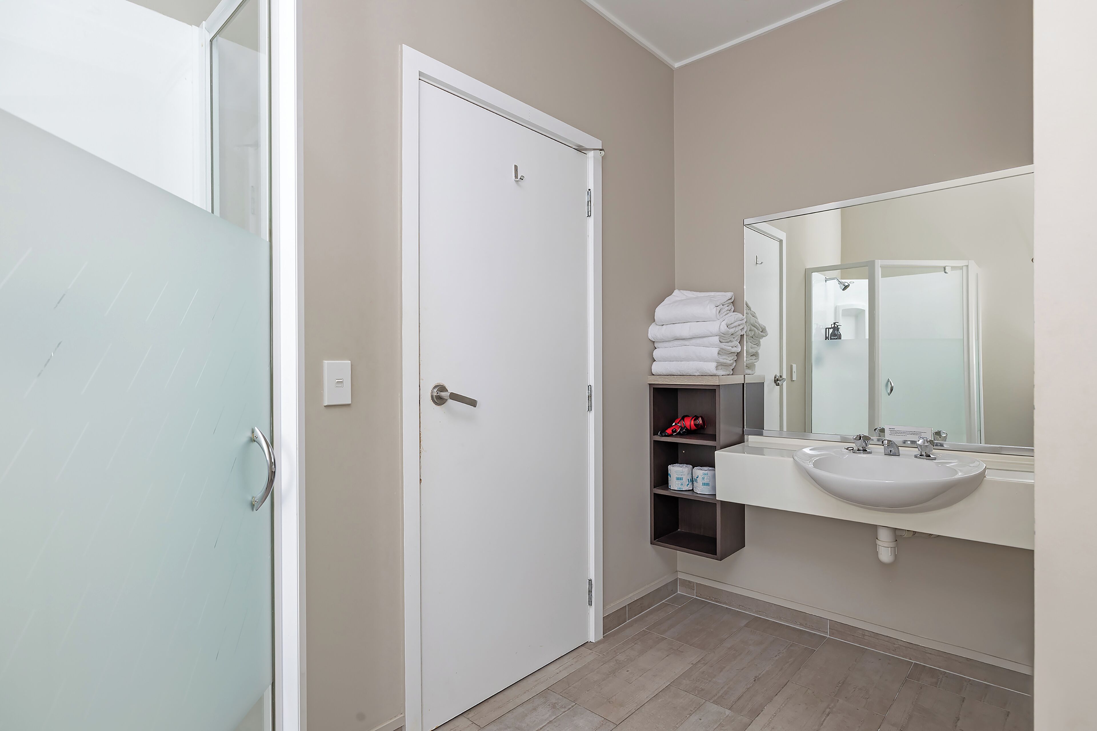 A bathroom with a white sink, a mirror, and a glass shower door.
