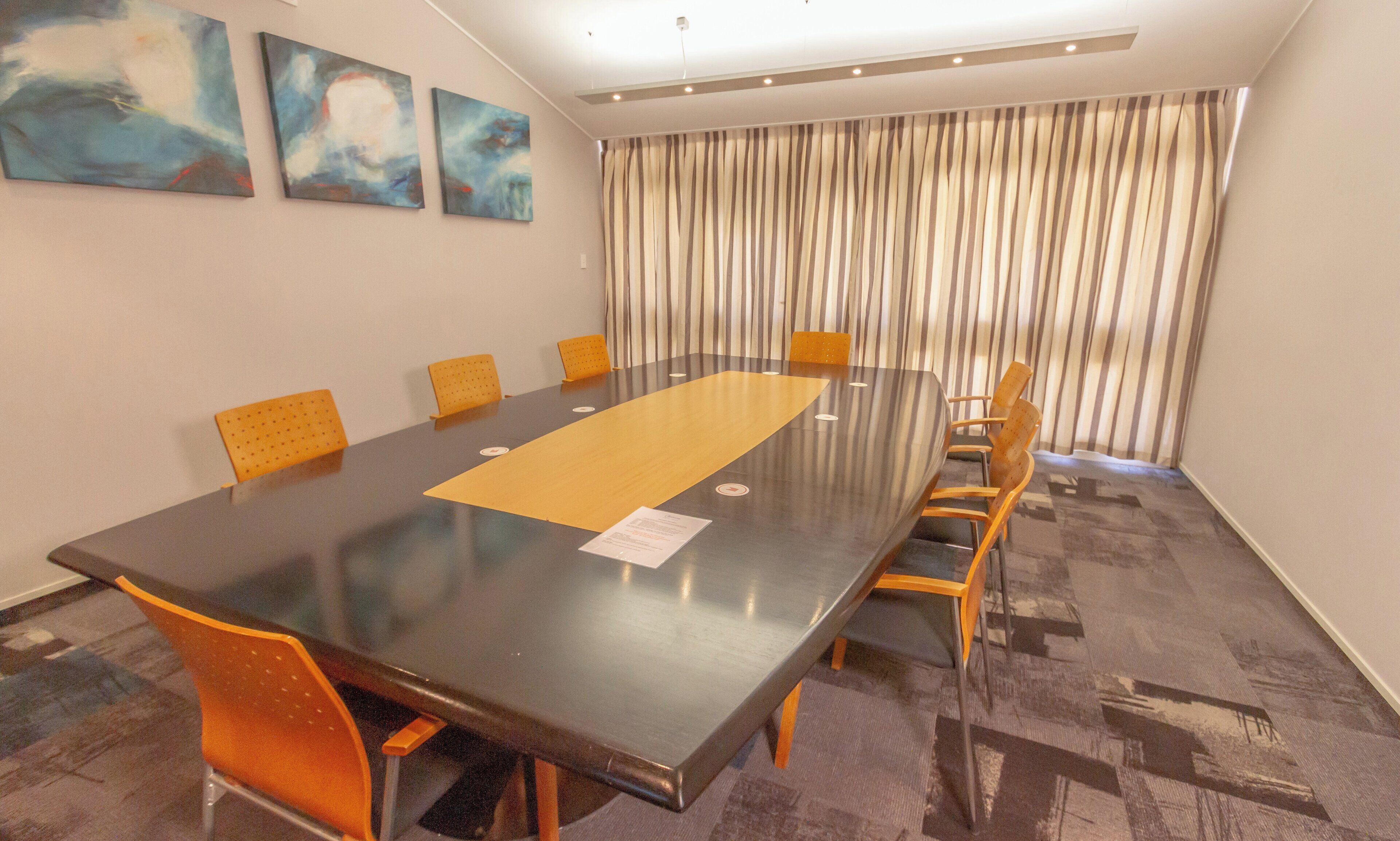 A conference room with a long table, chairs, and abstract paintings on the wall.