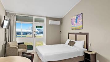 Une chambre d’hôtel avec un lit, une chaise, une table, un appareil de climatisation et un tableau au mur.