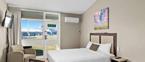 Una habitación de hotel con una cama, una silla, una mesa, un equipo de aire acondicionado y un cuadro en la pared.