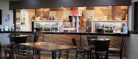 A bar area with multiple seating arrangements and a variety of bottles on shelves.