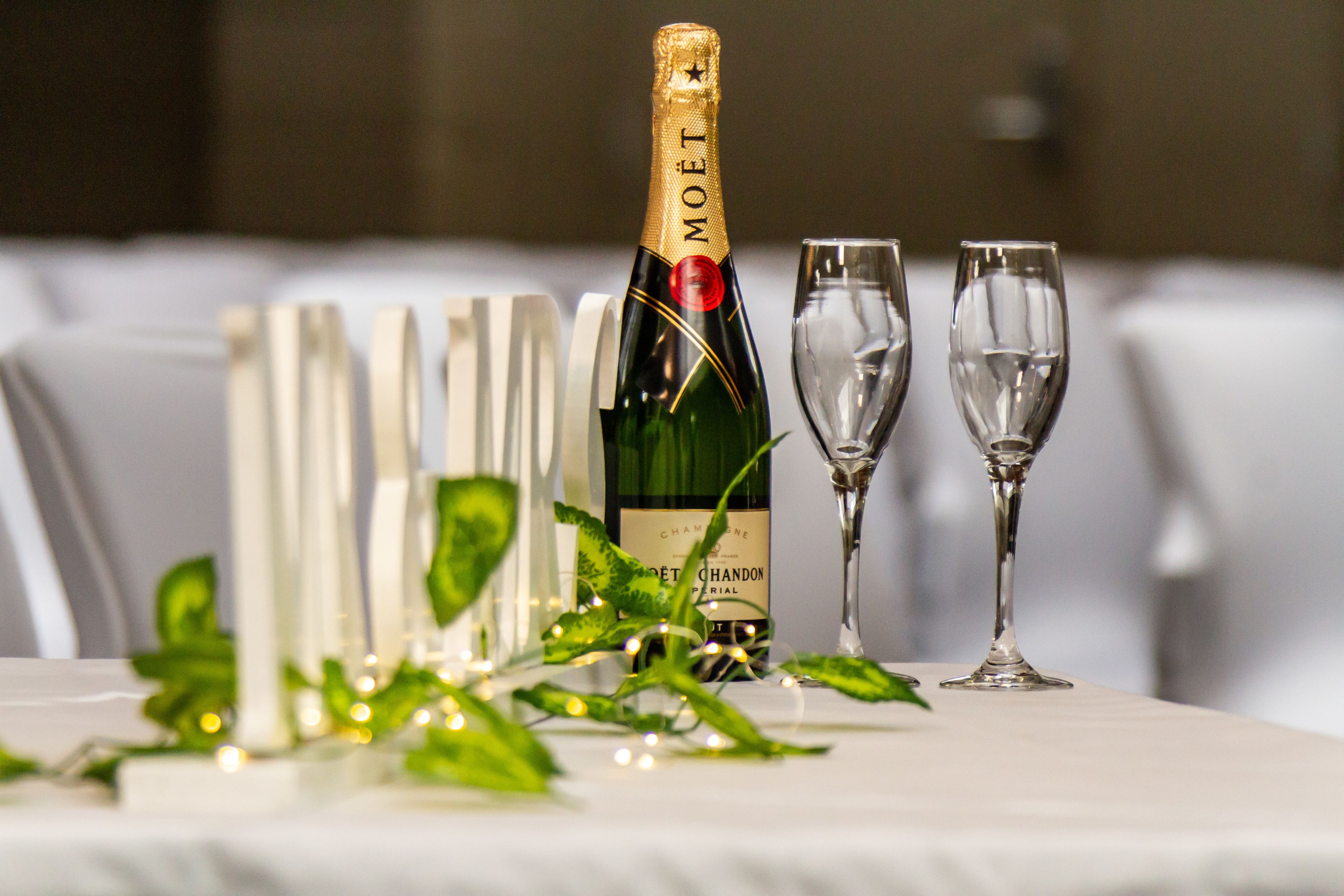 Un tavolo apparecchiato con una bottiglia di champagne Moët, due calici e un'elegante composizione di verde e luci.