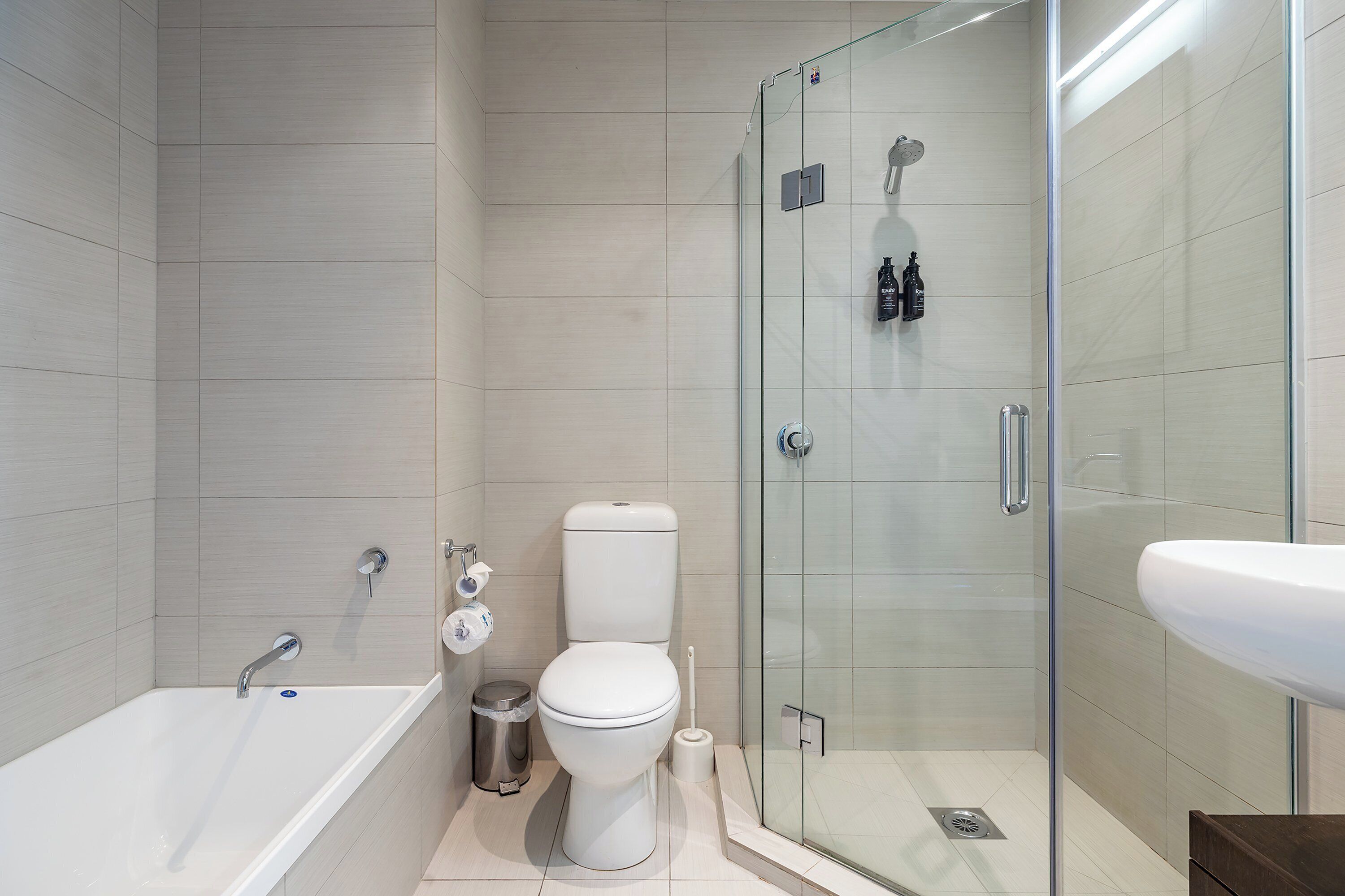 Un baño moderno con ducha envuelta en vidrio, una bañera blanca y un lavamanos.