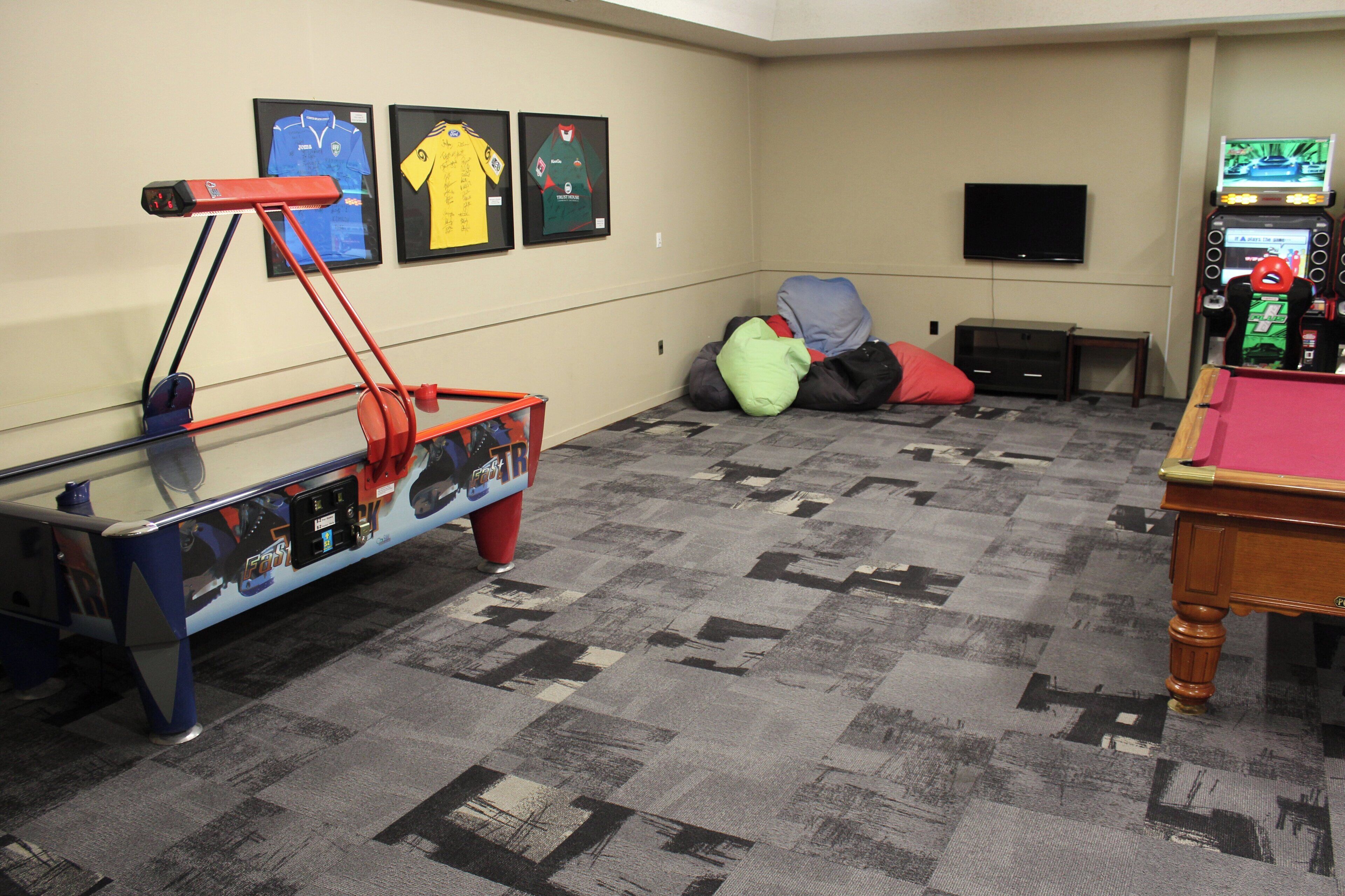 A room with a pool table, a ping pong table, a television, and framed sports jerseys on the wall.