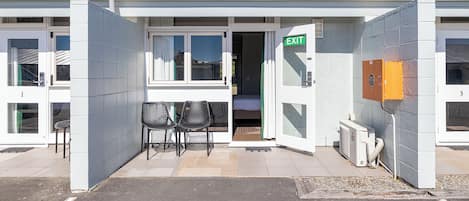 Un edificio con una señal de salida, un espacio exterior techado con sillas y una puerta que da al interior.