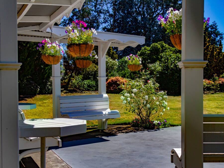 Un espacio cubierto con un banco blanco y macetas colgantes de flores.