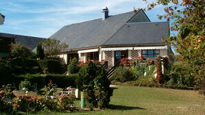 Une maison avec un toit en pente, une cheminée et un porche couvert agrémenté de plantes en pot.