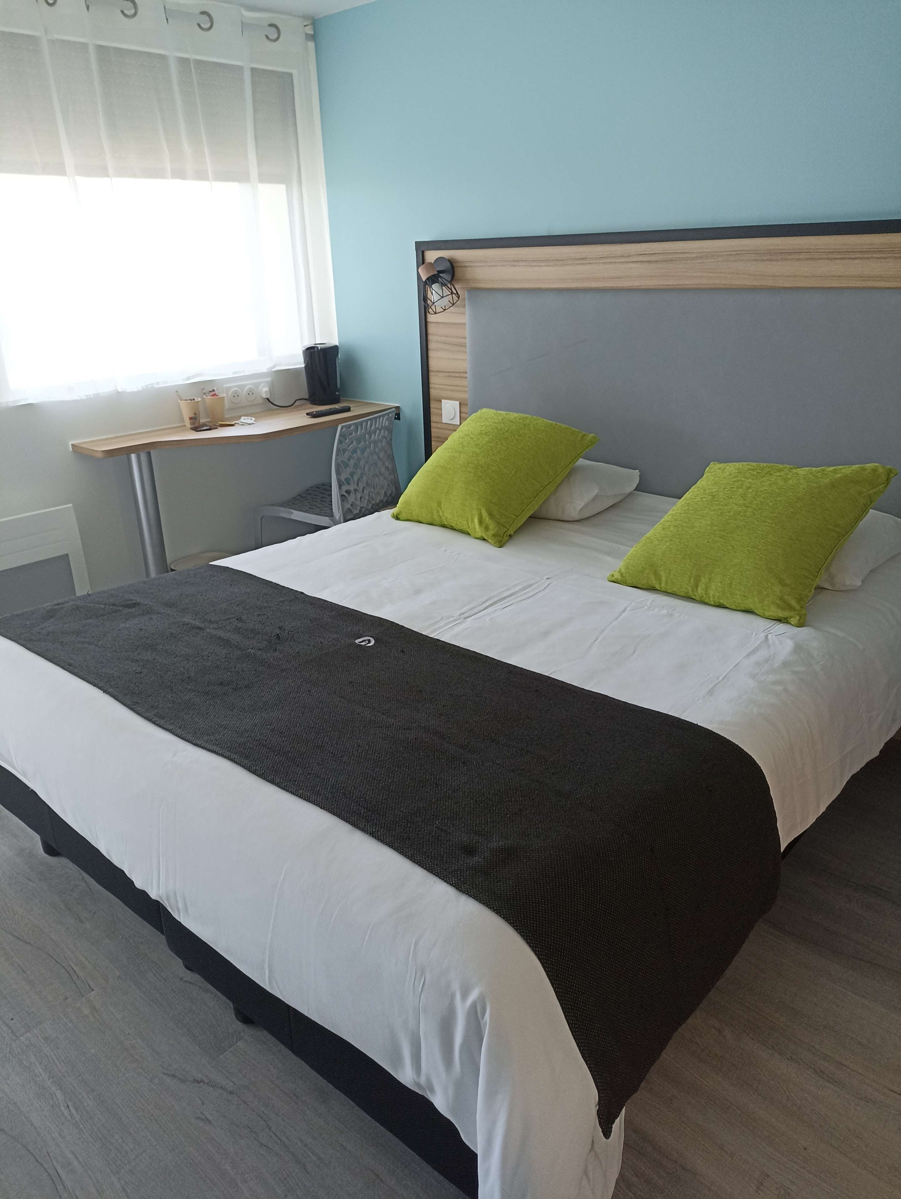 A neatly made bed with white and black bedding, two green pillows, and a wooden headboard.
