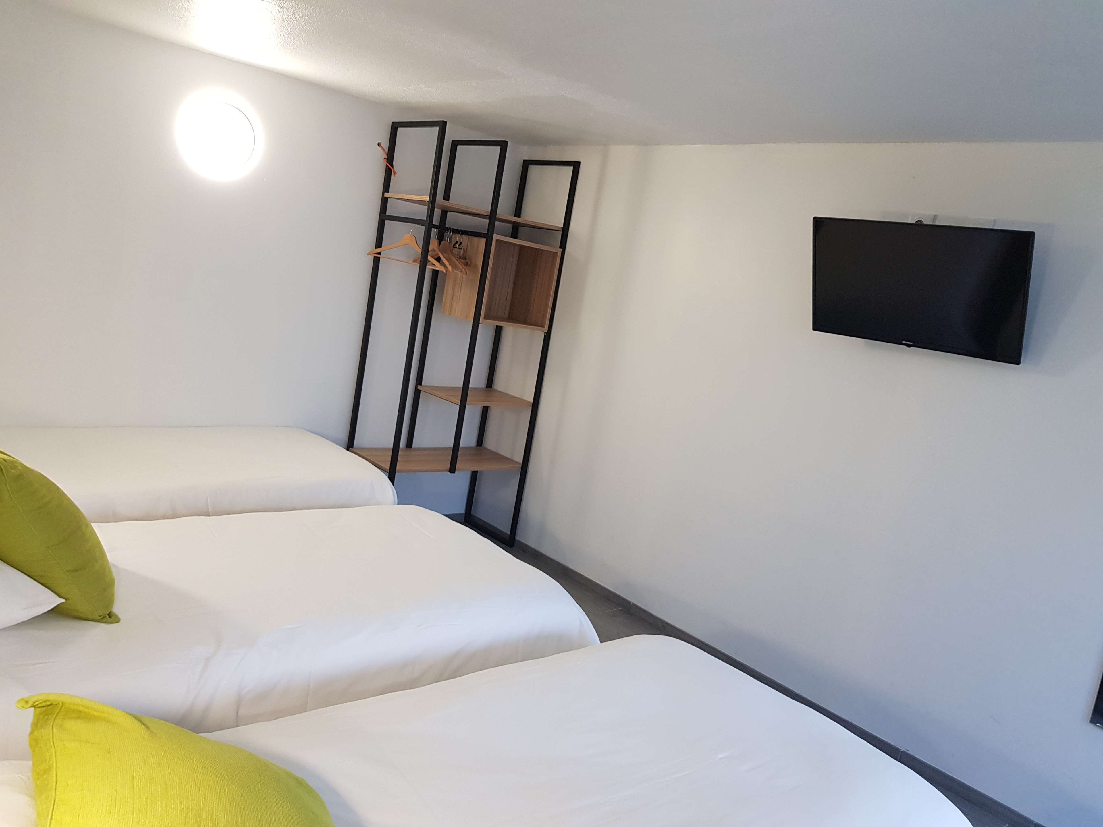 Habitación de hotel con dos camas, un televisor montado en la pared y una estantería de madera.