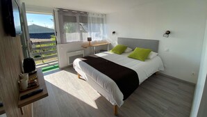 Une chambre à coucher avec un lit, une table de chevet, un téléviseur et une fenêtre avec des rideaux.
