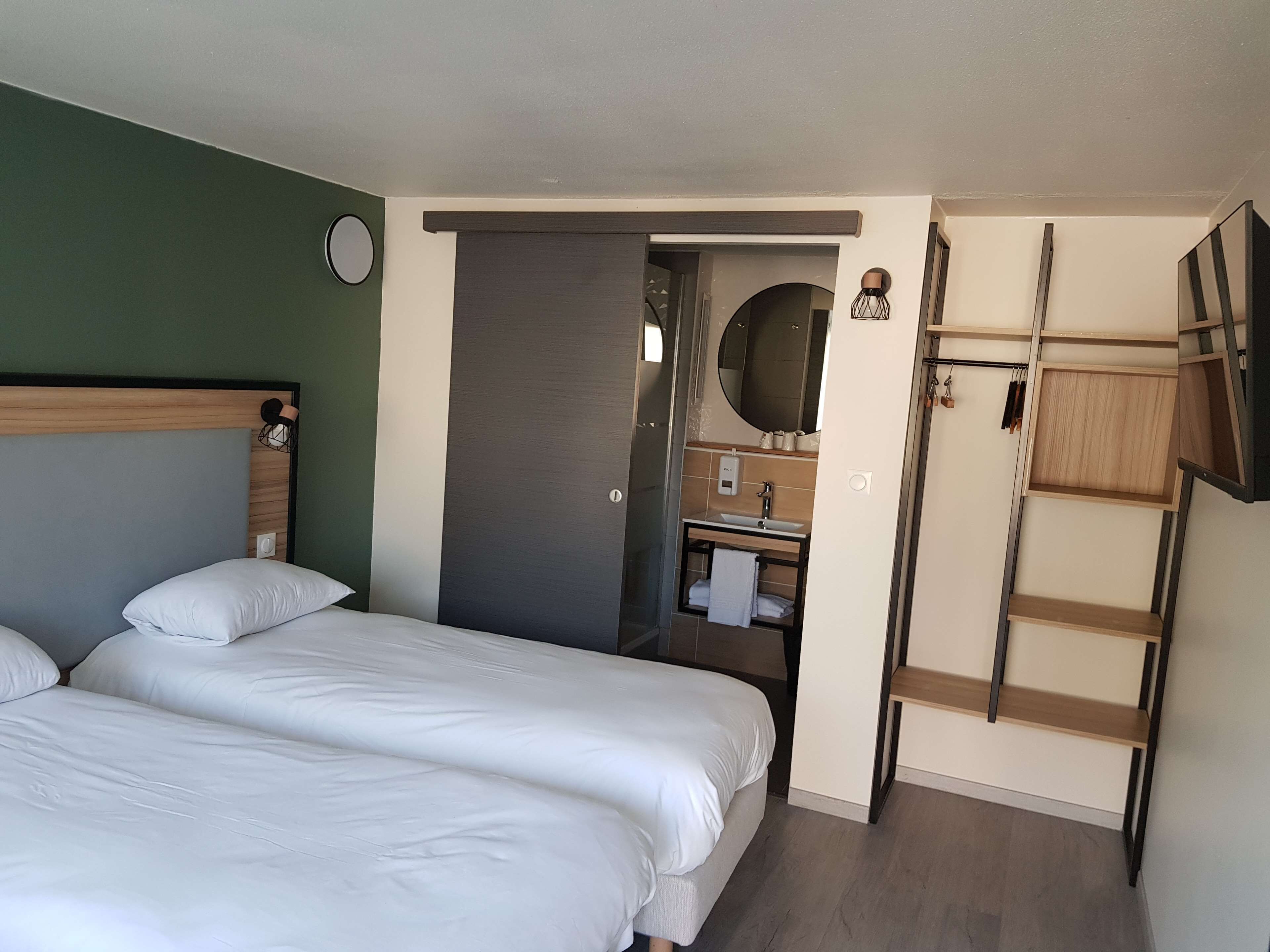 Quarto de hotel com duas camas, banheiro com pia e espelho, e uma escada de madeira.