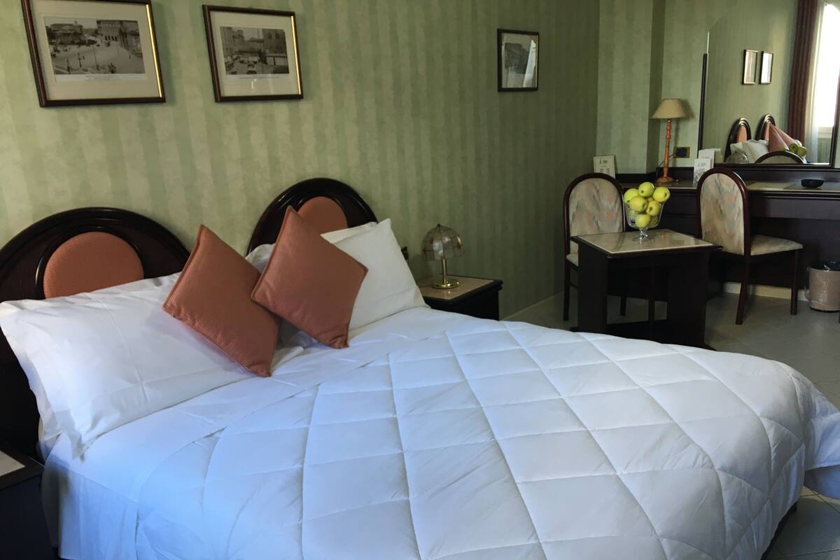 A hotel room with a large bed, a desk, a chair, and a mirror.