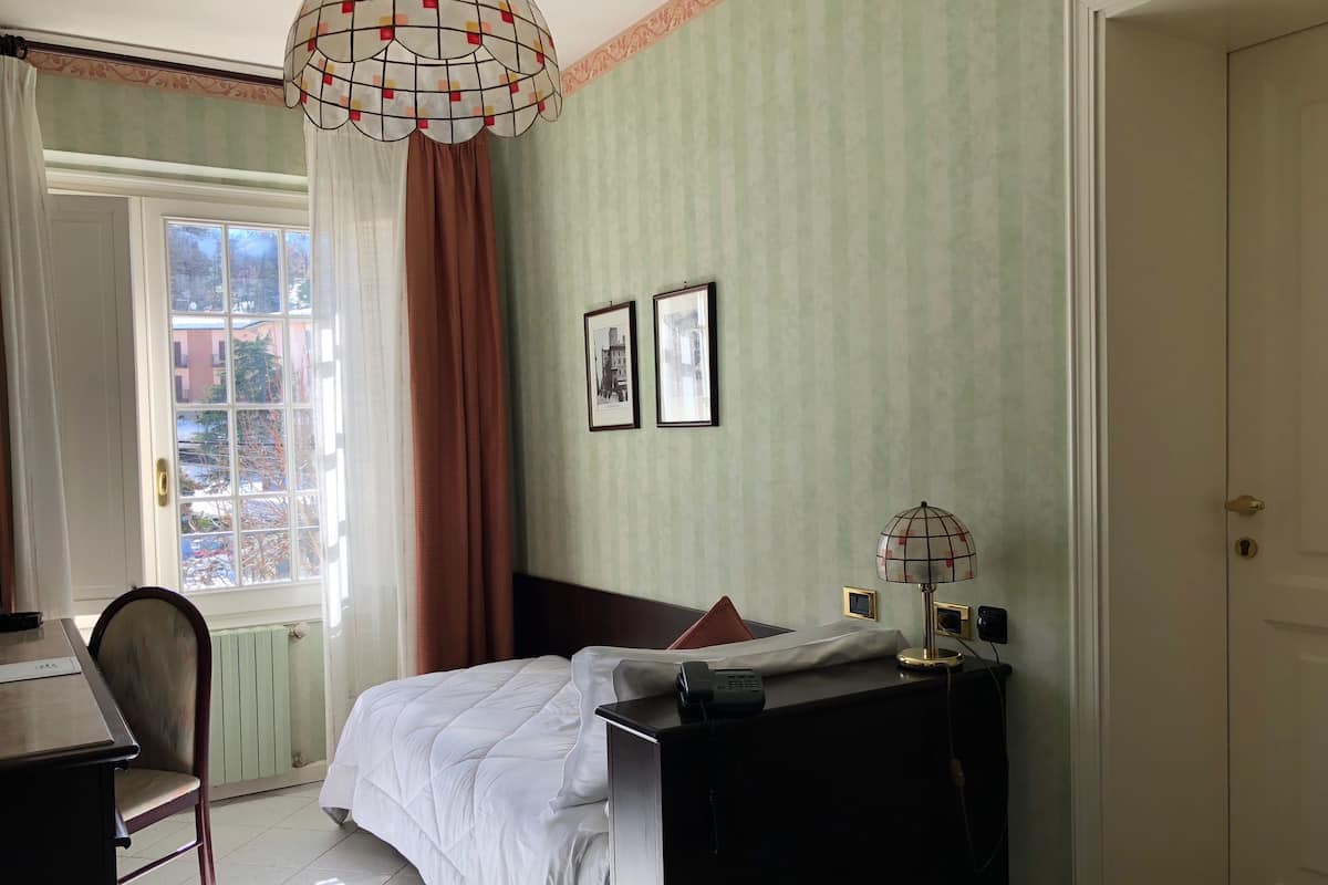 A hotel room with a bed, a desk, a chair, a lamp, and a window with curtains.