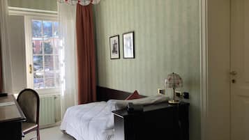 Habitación de hotel con cama, escritorio, silla, lámpara y ventana con cortinas.