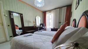 Habitación de hotel con dos camas, un escritorio, una silla, una lámpara y un espejo grande.