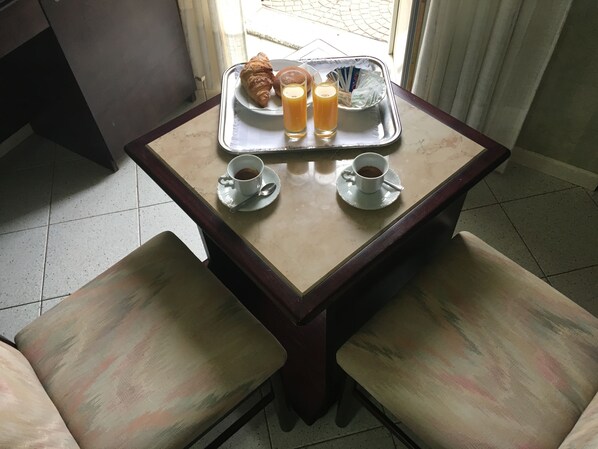 A breakfast tray with croissants, juice, and coffee on a table with two cushioned chairs.