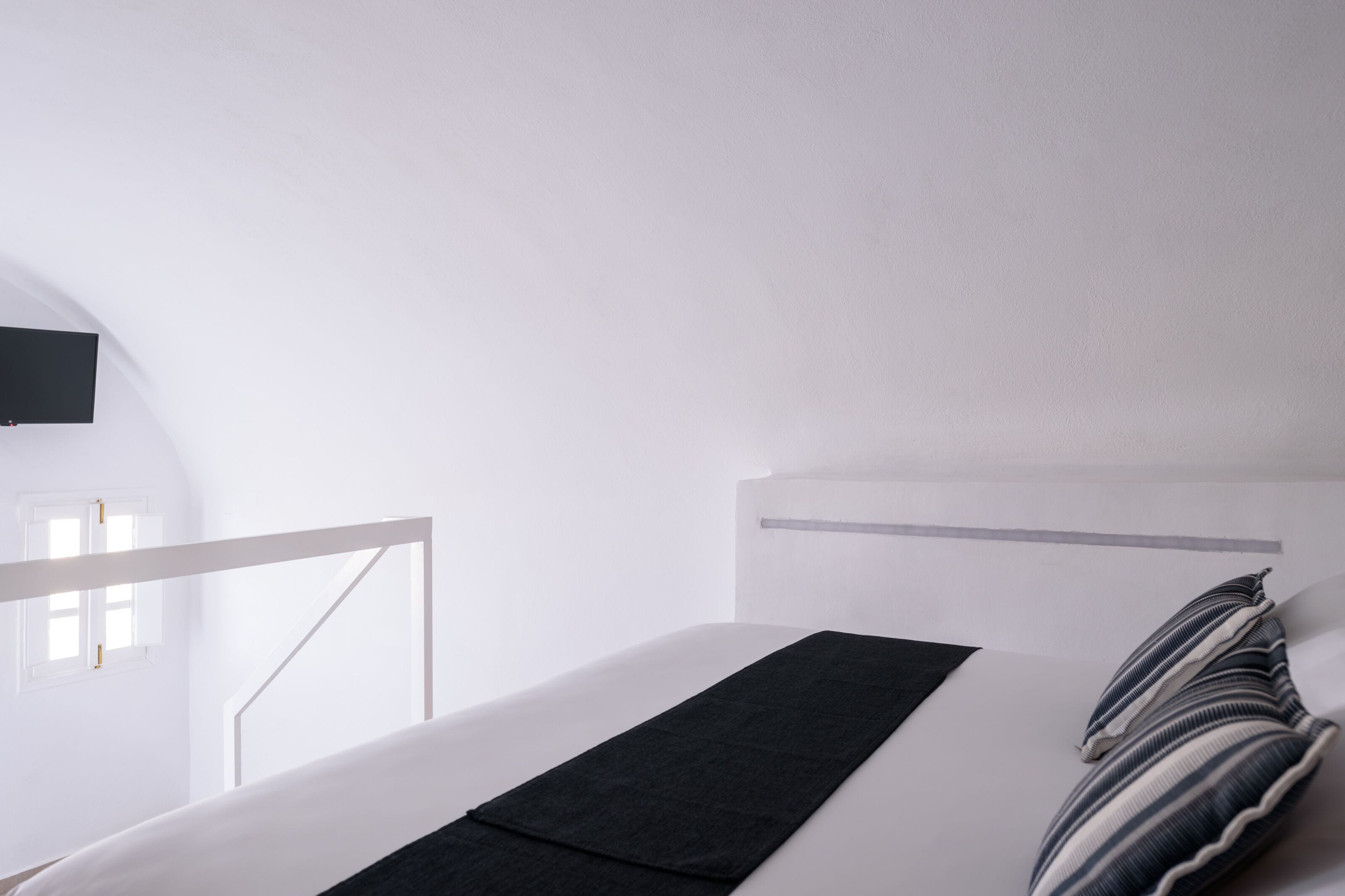 A hotel room with a bed, a flat-screen TV mounted on the wall, and a window with a view of the outside.